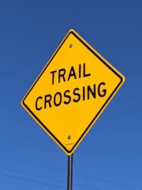 Low angle view of road sign against clear blue sky