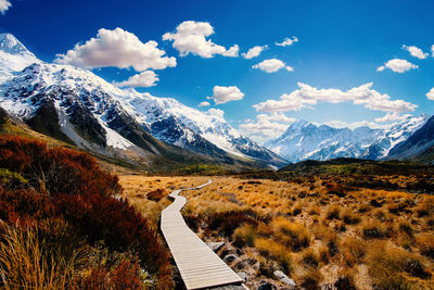 Boardwalk leading towards mountains against sky during winter