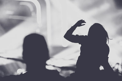 Silhouette woman with arms outstretched standing at music concert