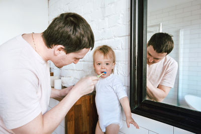 Man brushing teeth of adorable baby