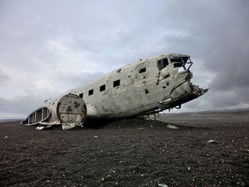 Abandoned airplane on field against cloudy sky