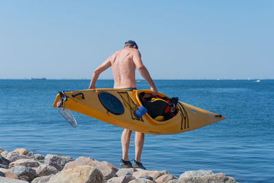 Rear view of shirtless man on rock against sea