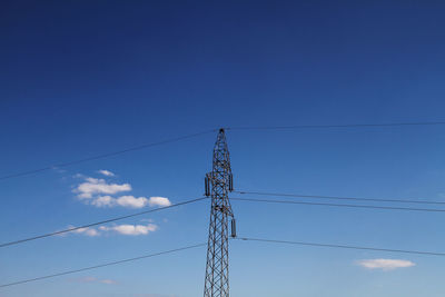 Low angle view of electricity pylon against blue sky