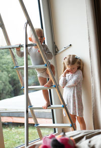 Baby boy standing by sister on ladder at home