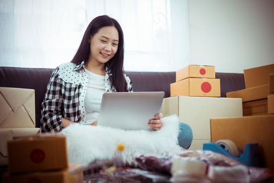 Smiling young woman using phone while sitting at home