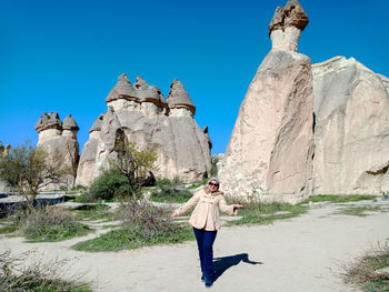 Woman standing by rock formation against clear blue sky