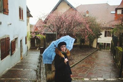 Portrait of woman holding umbrella while standing in front of building