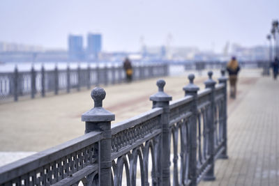 Railing on pier by sea against sky in city