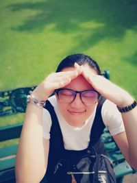 High angle view of young woman shielding from sunlight on bench in park