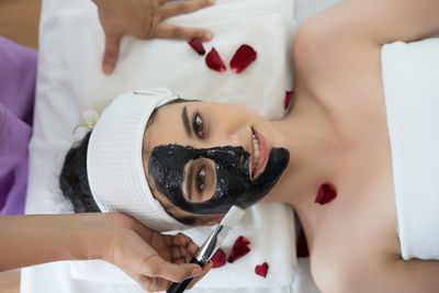 Cropped hand of massage therapist applying facial mask on young woman face in spa