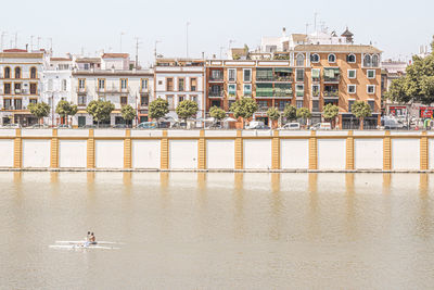 Men practicing canoeing on the river with colonial-style houses at triana