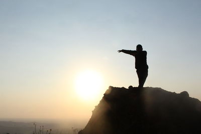 Silhouette man standing on rock against sky during sunset