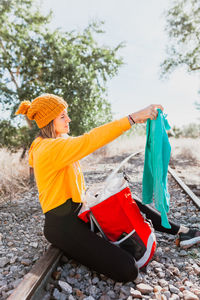 Woman trekking rests on an abandoned railway track looking for something in her backpack