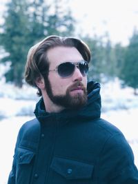 Bearded man wearing sunglasses against trees during winter