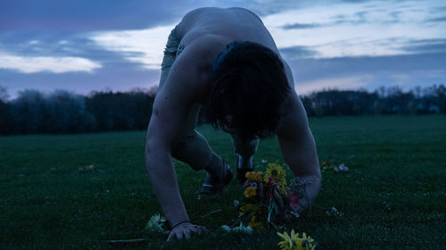 Shirtless man holding flowers on grassy land at sunset