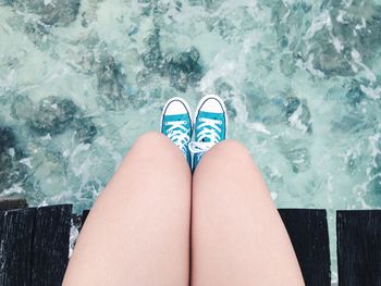 Low section of young woman sitting on pier over sea