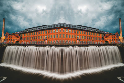 View of fountain by building against cloudy sky