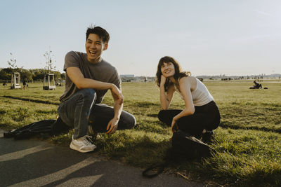 Happy friends crouching on grass against sky in park