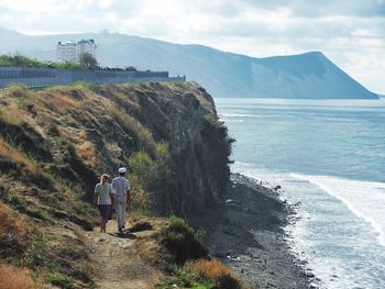 Rear view of man and woman walking on hill by sea against sky