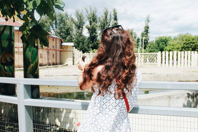 Rear view of woman standing by railing against sky