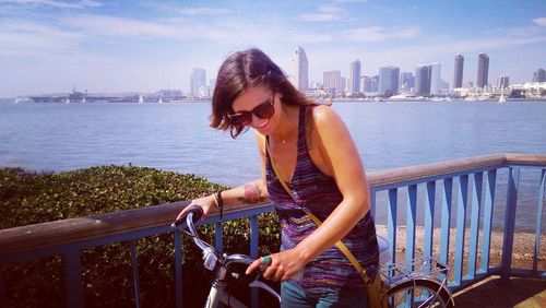 Woman on railing by sea against cityscape