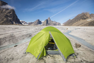 Mountaineering tent set up on glacier below dramatic mountain peaks.