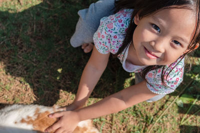 High angle portrait of cute smiling girl holding cat while crouching on grassy field