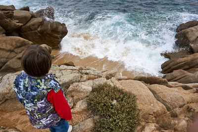 Rear view of boy standing on rock at beach