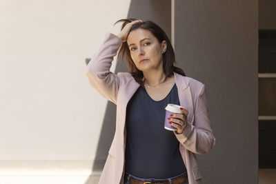 Puzzled sad mature 40 yo woman holds cup of coffee, looking at camera outside, tired, worried