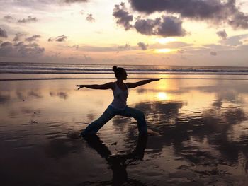 Full length of woman exercising at beach against sky during sunset