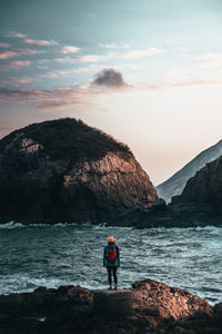 Man standing on rock by sea against sky during sunset