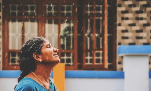 Mature woman enjoying rain by building in city