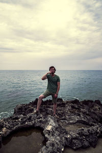 Full length of man on rock in sea against sky