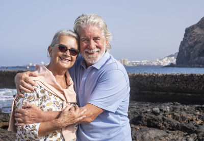 Portrait of smiling couple standing on rock against sea and sky