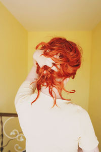 Rear view of woman standing against wall at home