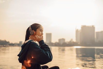 Woman standing by river against sky in city
