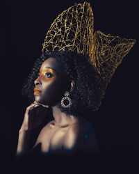 Close-up of woman with make-up looking away against black background