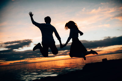 Silhouette woman jumping on beach against sky during sunset