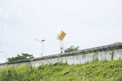 Low angle view of woman carrying cardboard box against sky