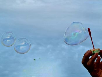Person holding bubbles against sky