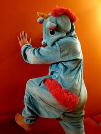 Side view of person wearing animal costume while standing by orange wall