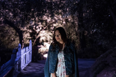 Woman standing against trees at night