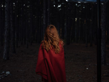 Rear view of woman standing by trees in forest