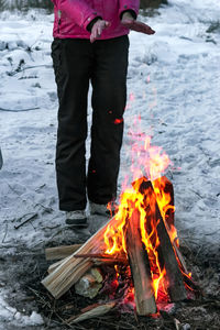 Woman by teepee campfire on snow at campsite in wild at dusk, winter camping at night