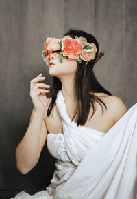 Young woman with flowers in front of face against wall