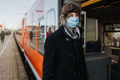 Portrait woman wearing mask standing by train on railroad station platform