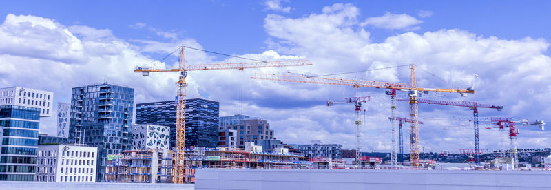 Low angle view of cranes at construction site against sky