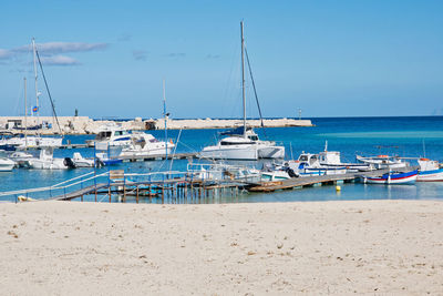 Sailboats moored at harbor against blue sky