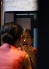 Rear view of woman applying make-up in front of mirror