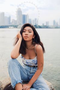 Portrait of beautiful young woman sitting or rock by sea